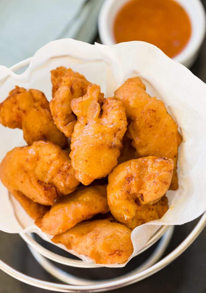 These homemade Chinese chicken fingers are JUST like from a restaurant. Crispy and golden on the outside and filled with juicy chicken on the inside. Perfect with sweet and sour sauce! Golden fried Chinese Chicken Fingers in a serving bowl with sweet and sour sauce in the background.