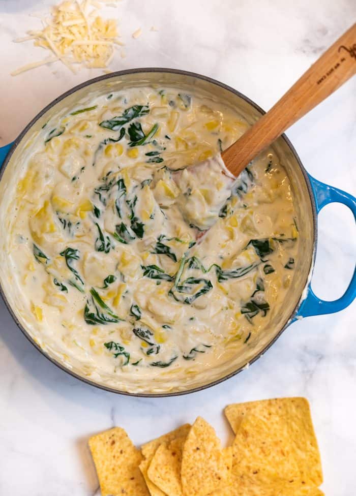 This ultra-creamy Spinach and Artichoke Dip tastes just like the Applebee's version! It's easy to make at home in under 30 minutes, just combine the ingredients until melted! This is perfect with tortilla chips, pita chips, crusty Artisan breads, and vegetables! | The Cozy Cook | #appetizer #dip #applebees #copycat #spinach #artichoke Spinach and Artichoke Dip in a Dutch oven on white granite with chips and cheese