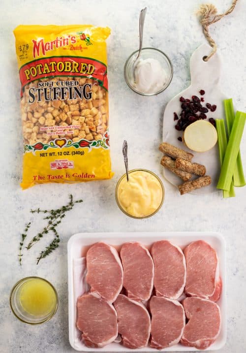 These easy-to-make Pork Chops are perfectly seasoned and stuffed with delicious sausage cranberry stuffing. They are then baked to perfection in just 20 minutes and pair perfectly with roasted potatoes and green beans. | The Cozy Cook | #PorkChops #Dinner Ovehead shot of bag of stuffing, Tray of uncooked Pork chops, and other stuffing ingredients