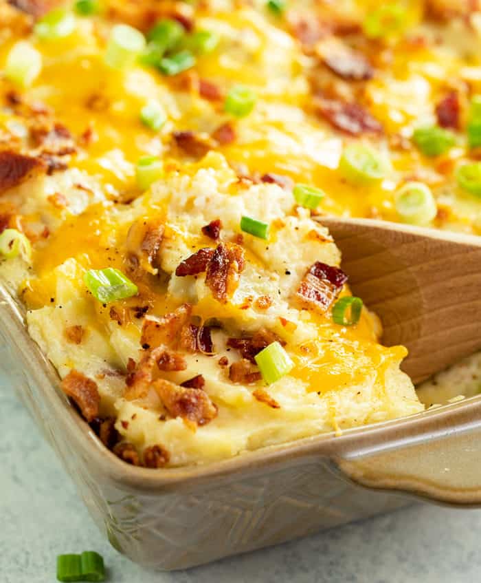 This Twice Baked Potato Casserole recipe from The Pioneer Woman is an easy make ahead side dish idea for Thanksgiving, Christmas, or any family dinner! #comfortfood #bacon #potatorecipes #mashedpotatoes #sides #holidayrecipes A close up image of a wooden spoon filled twice baked potato casserole in a casserole dish.