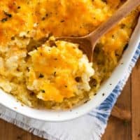 Overhead view of a white casserole dish filled with hashbrown casserole with a wooden spoon scooping it up.