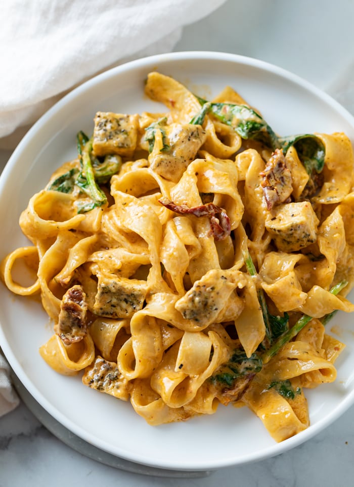 A white plate topped with creamy Tuscan Chicken Pasta with spinach and chicken.