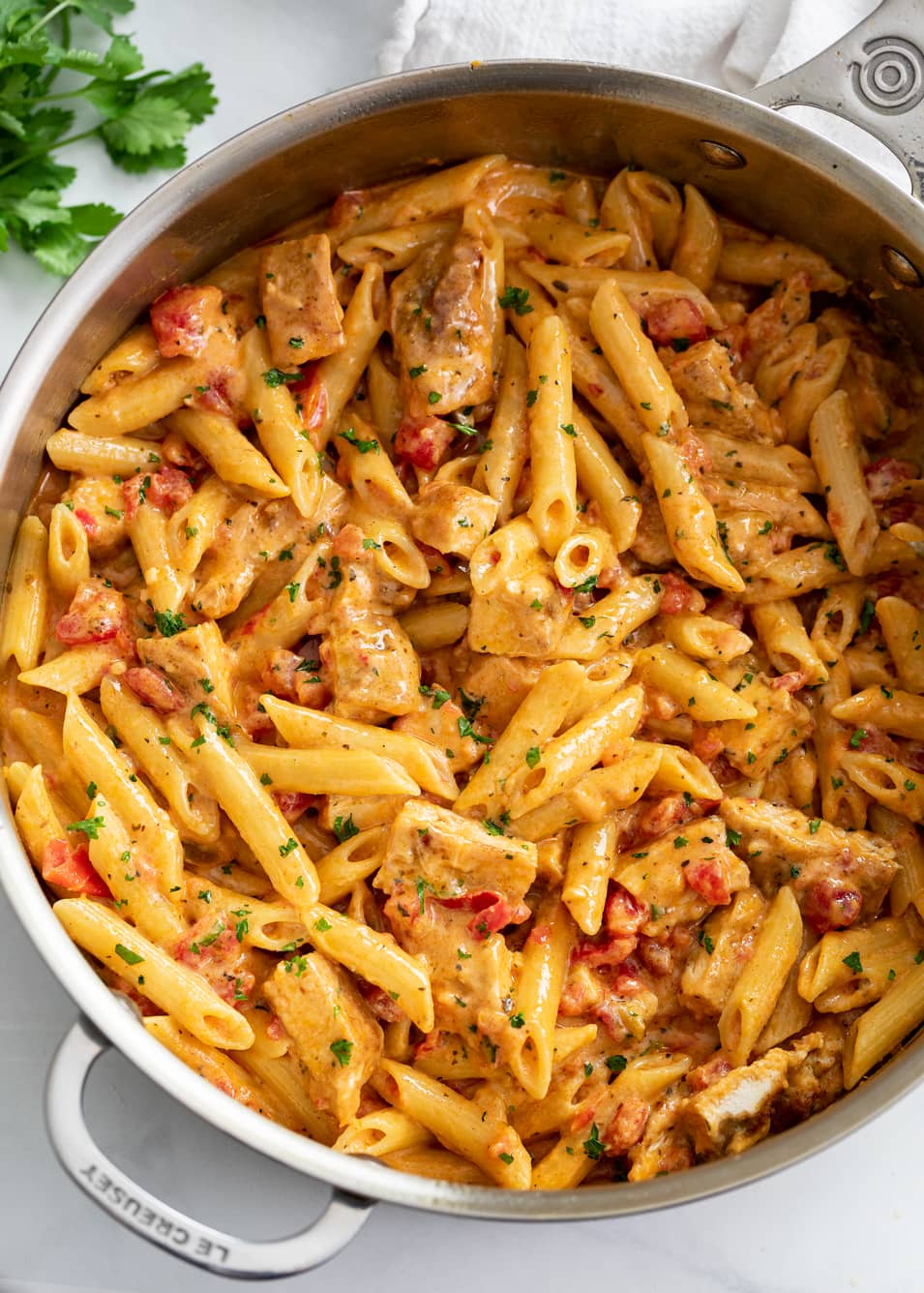 Cajun Chicken Pasta in a skillet with penne pasta, cream sauce, and tomatoes.
