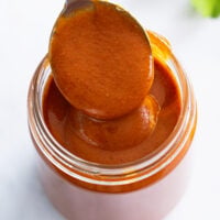 A spoon scooping Homemade Enchilada Sauce from a glass jar.