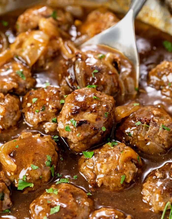 A skillet with meatballs and gravy topped with fresh parsley.