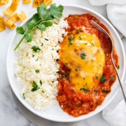 A white plate with Salsa Chicken on it next to white rice with a cilantro garnish.