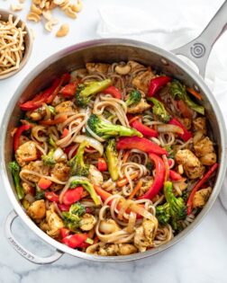 A skillet with Chicken Noodle Stir Fry with Chow Mein Noodles and Cashews on the side.