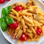 Caprese pasta on a white plate with cherry tomatoes and basil.