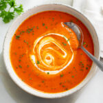 Roasted Red Pepper Pasta with a swirl of cream on top and a spoon on the side.