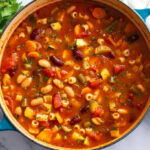 A soup bowl filled with Minestrone Soup with vegetables and beans.