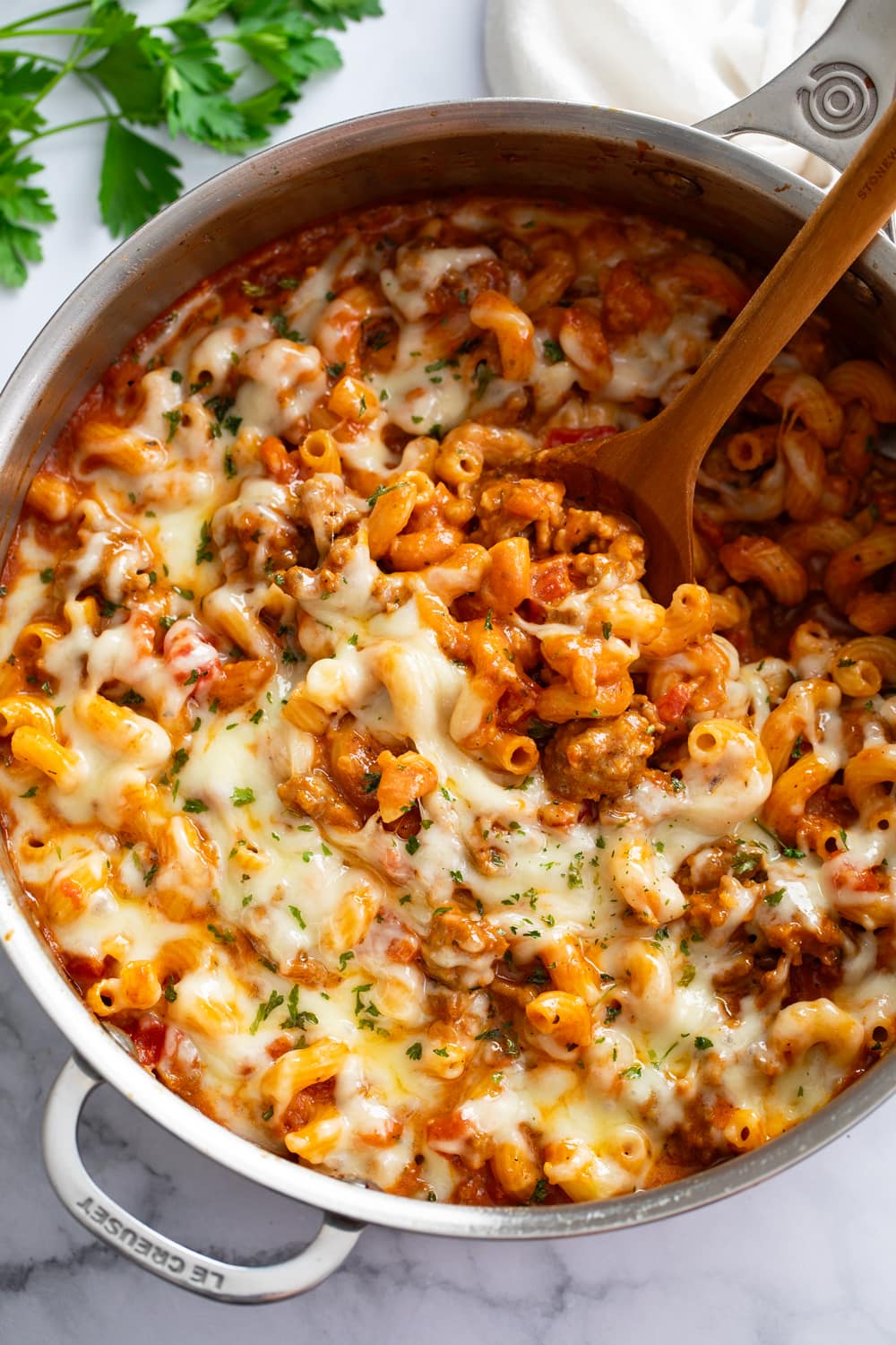 Italian Sausage Pasta in a skillet with a wooden spoon scooping it up.