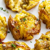 A Smashed Potato on a white plate with fresh thyme and seasonings.