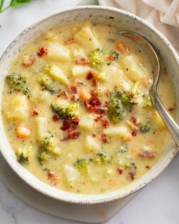 Broccoli Potato Soup in a white bowl with bacon on top and a spoon on the side.