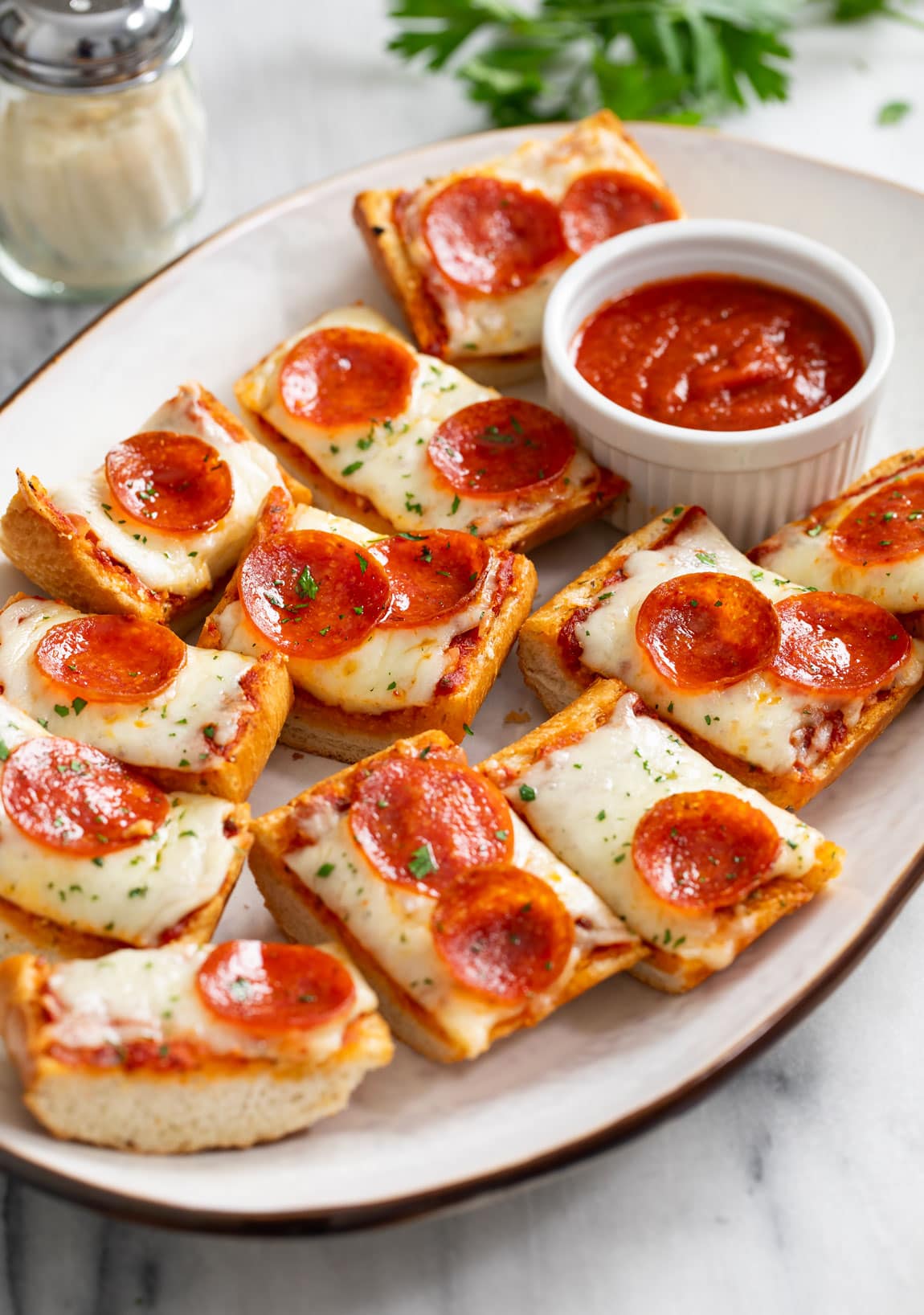 Slices of Pepperoni French Bread Pizza on a white platter with sauce on the side.