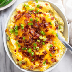 Loaded Mashed Potatoes in a white bowl with melted cheese, crispy bacon, and sliced green onions.