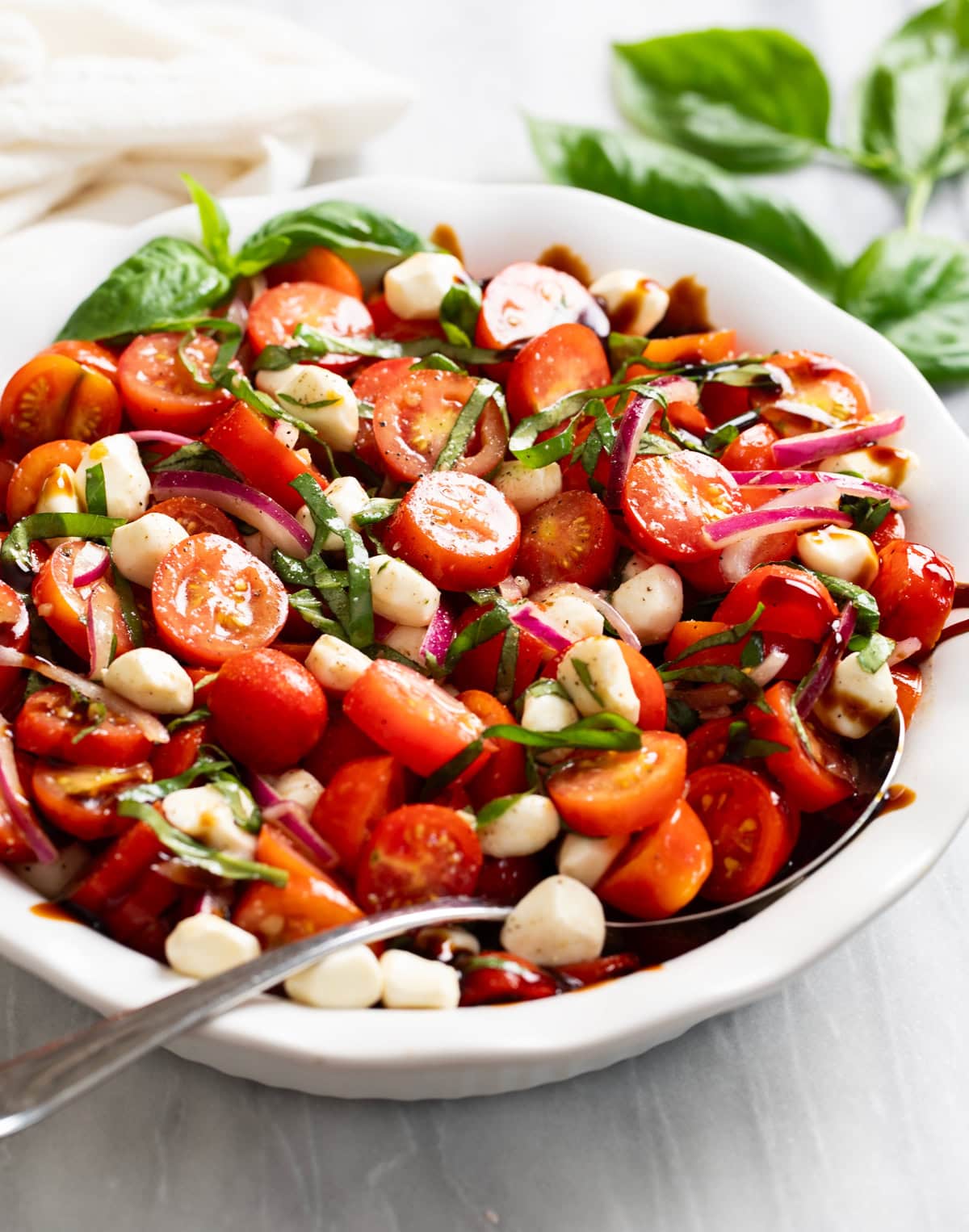 Side view of Tomato Salad in a white bowl with a spoon on the side.