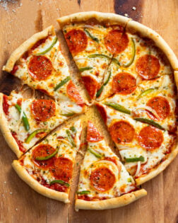 Slices of Cast Iron Skillet Pizza with pepperoni, peppers, and onions on a wooden surface.