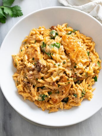 A white bowl filled with Marry Me Chicken Orzo in a tomato cream sauce with sun-dried tomatoes and spinach.