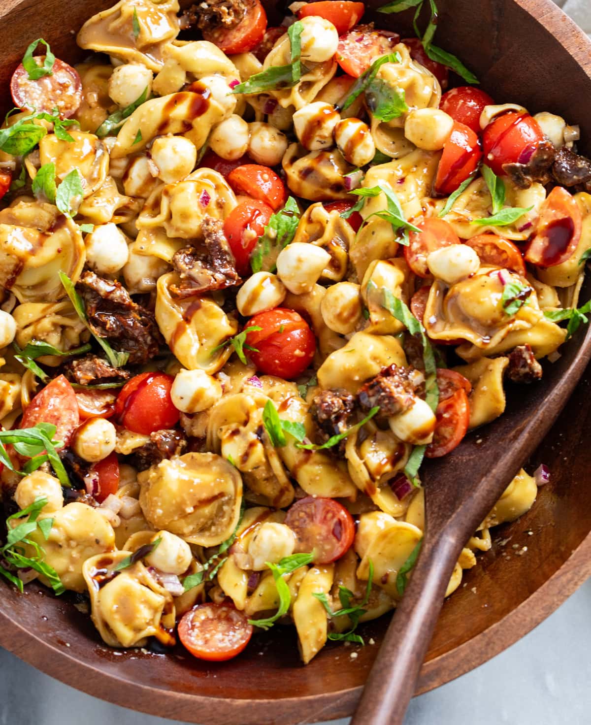A wooden bowl filled with Caprese Pasta Salad with fresh basil and balsamic glaze on top.