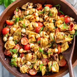 Caprese Pasta Salad in a wooden bowl with balsamic glaze drizzled on top with fresh basil.